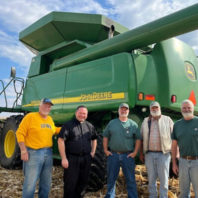 Five men stand in front of a combine in a corn field