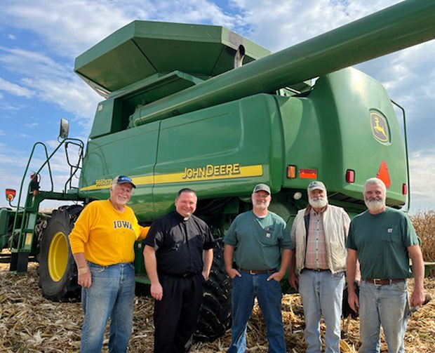 Five men stand in front of a combine in a corn field